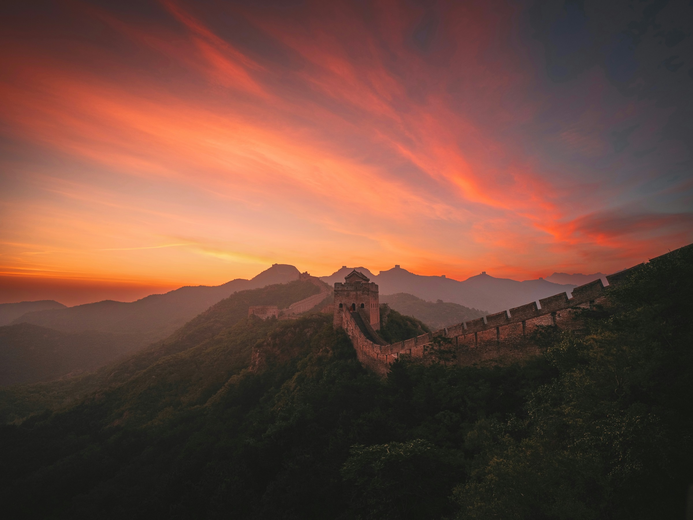 The Great Wall and watchtowers at Jinshanling beneath a vivid orange and pink sunset sky The Great Wall and watchtowers at Jinshanling beneath a vivid orange and pink sunset sky