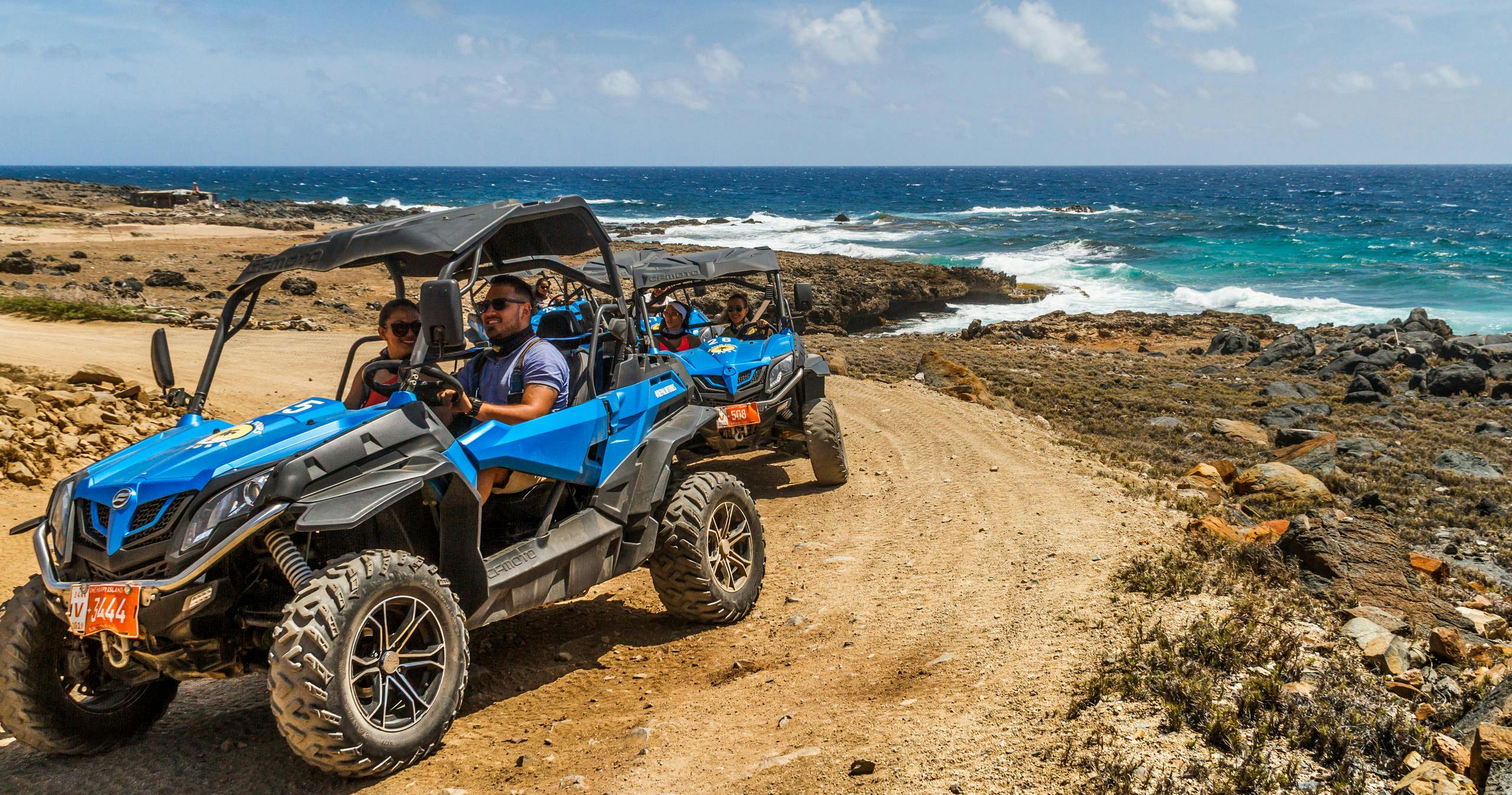 UTV convoy driving along Aruba’s rugged north coast with rocky cliffs and turquoise Caribbean waves