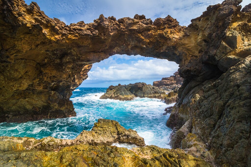 Natural rock bridge on Aruba's rugged east coast with waves crashing below