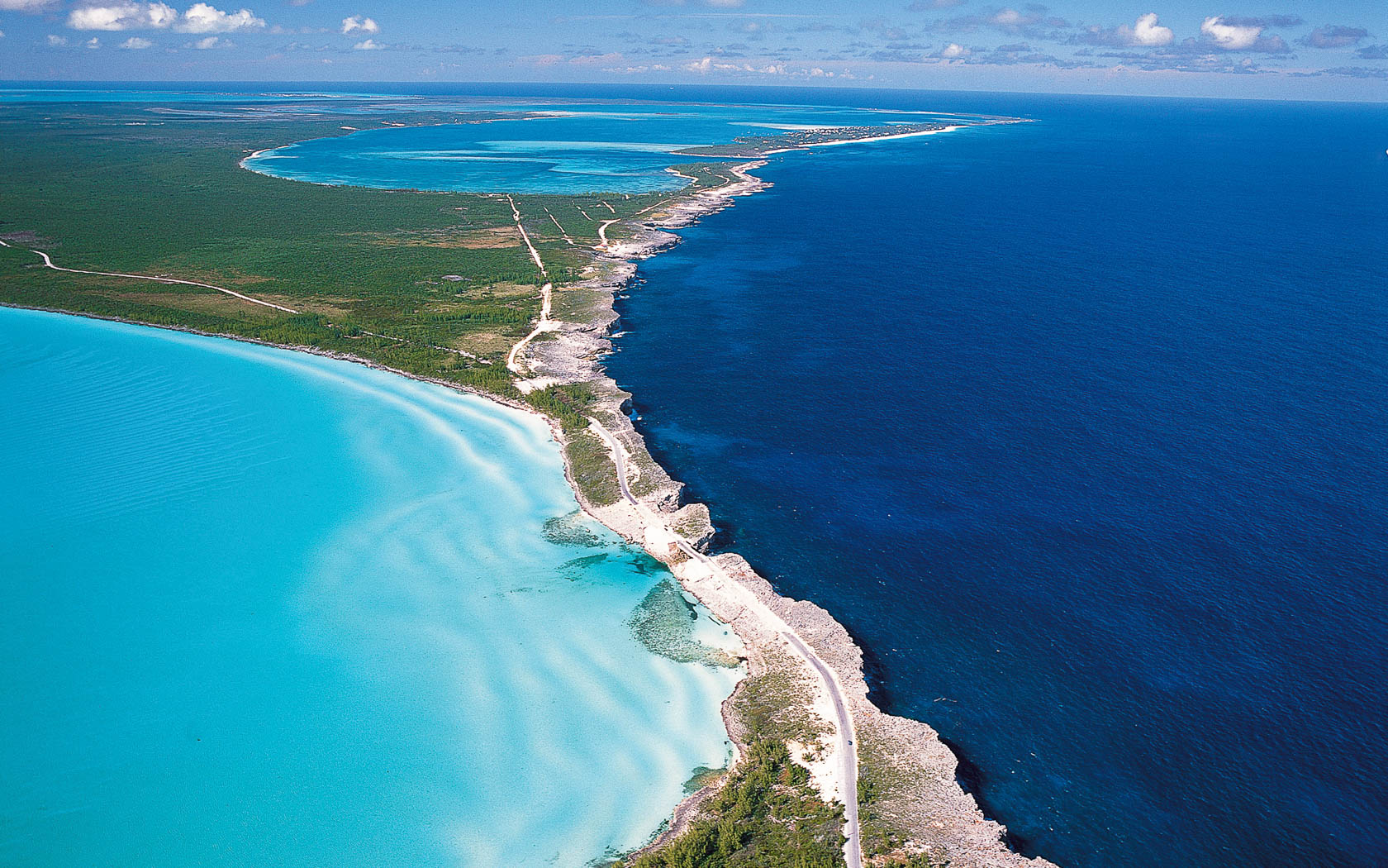 Aerial view of a coastal road in the Bahamas running between shallow turquoise water and deep blue ocean