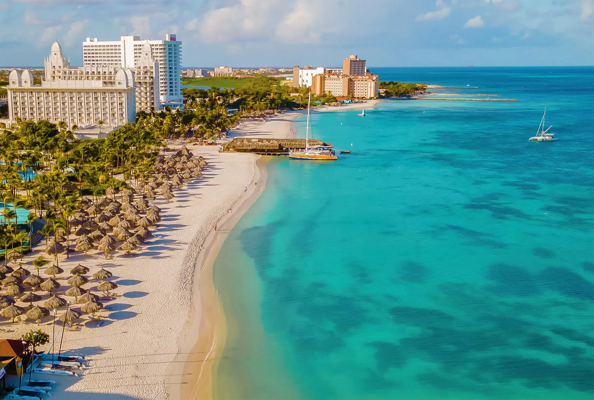 Wide white-sand beach in Aruba with calm turquoise sea and sun loungers