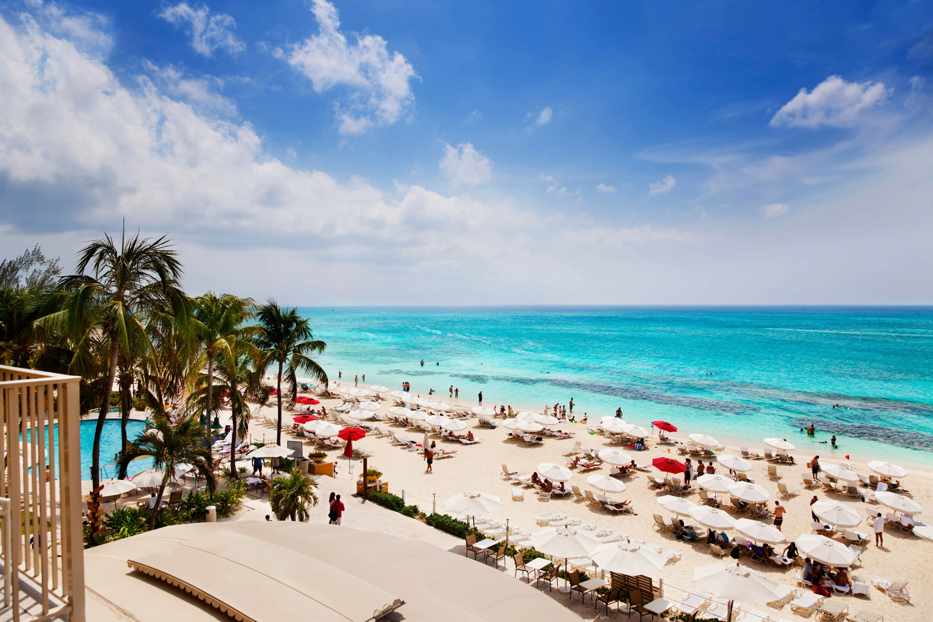 View of Seven Mile Beach in Grand Cayman with turquoise water, white sand, palm trees and beach umbrellas