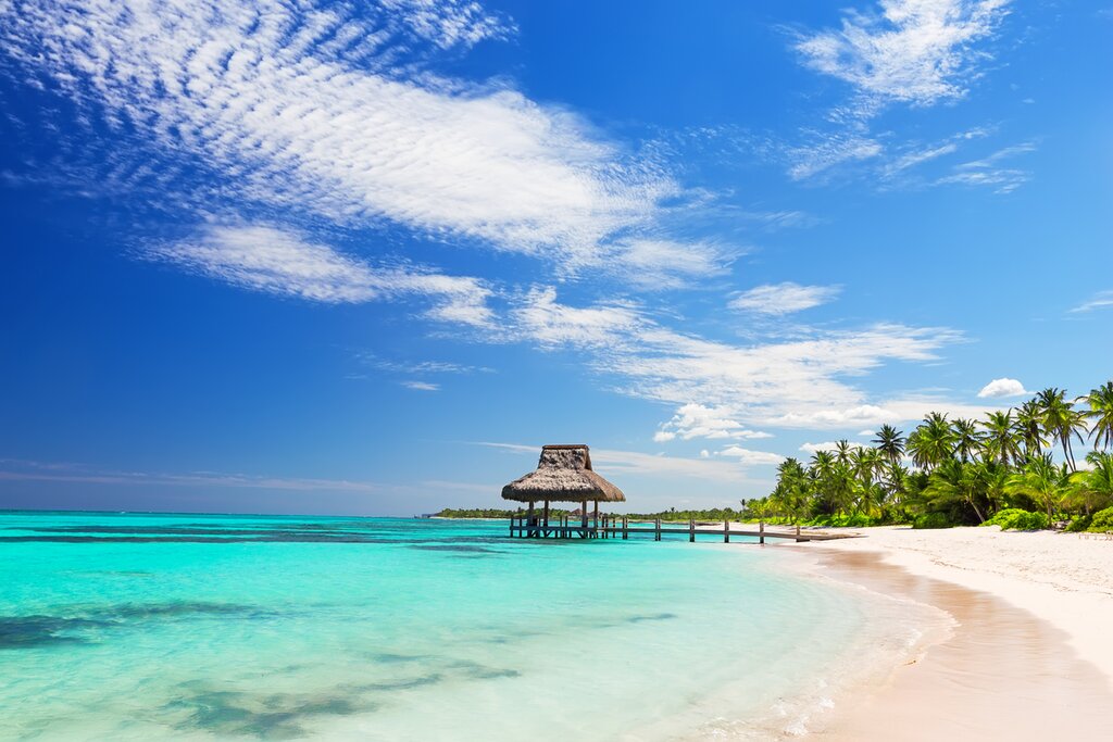 Tropical beach in the Dominican Republic with white sand, turquoise water, palm trees and a wooden pier over calm Caribbean sea