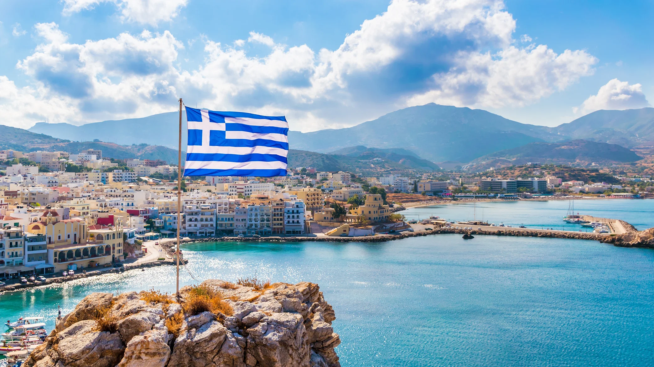 Greek flag overlooking a coastal town and harbor in Greece