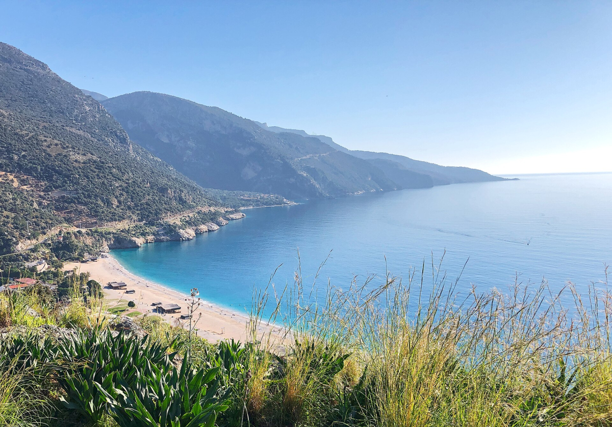 A sandy beach and blue sea below the mountains near Ölüdeniz