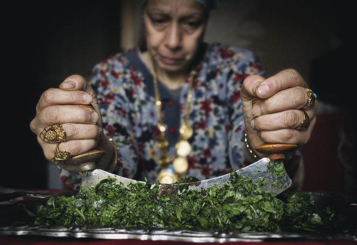 Cook chopping green molokhia leaves with a curved blade Cook chopping green molokhia leaves with a curved blade