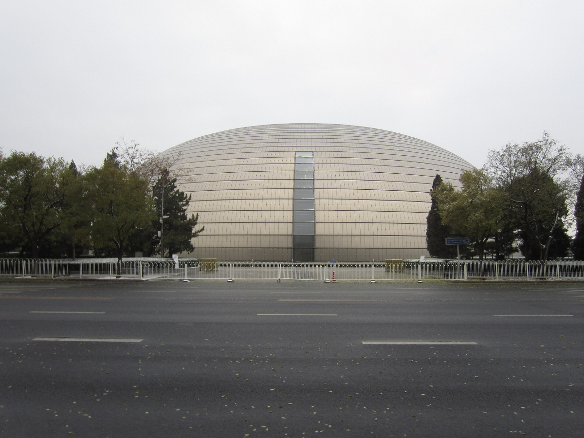The curved National Centre for the Performing Arts exterior behind trees in Beijing The curved National Centre for the Performing Arts exterior behind trees in Beijing