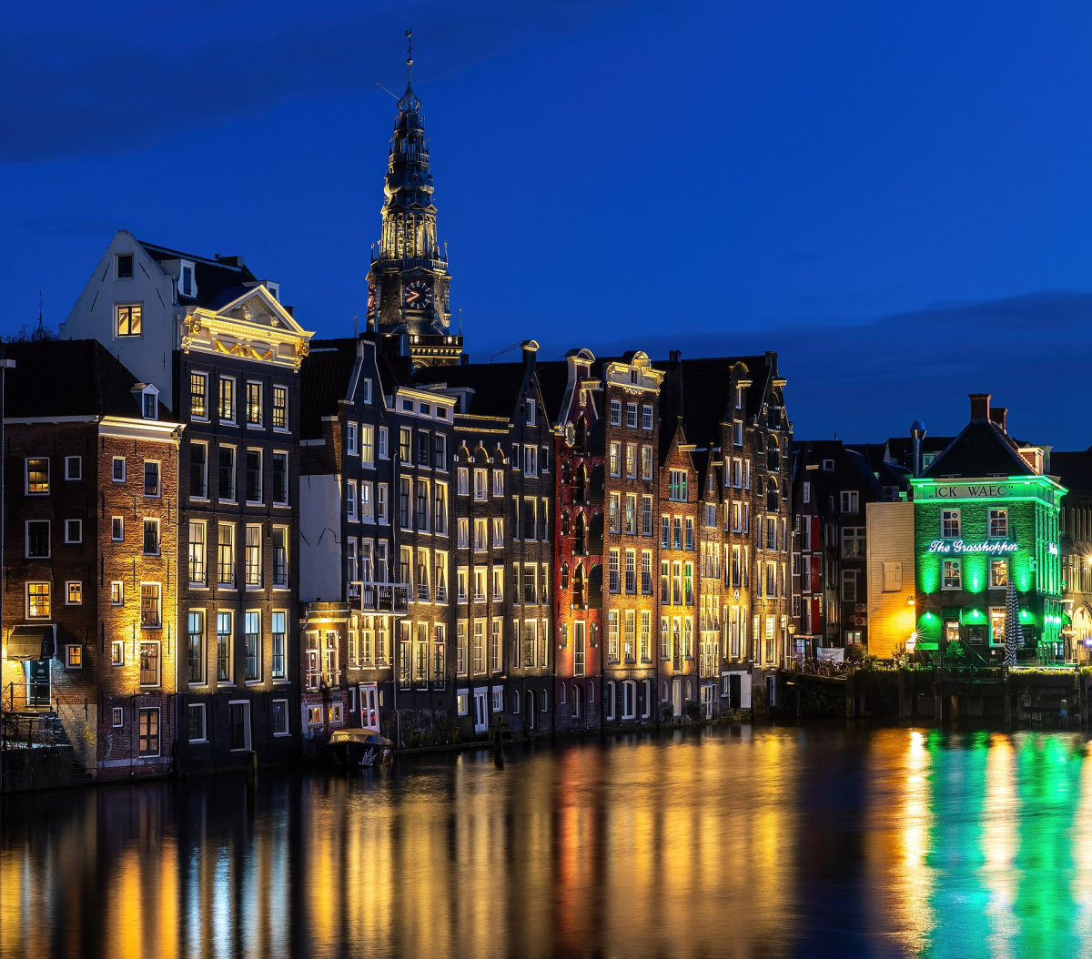 Illuminated canal houses and the Oude Kerk skyline at Damrak.