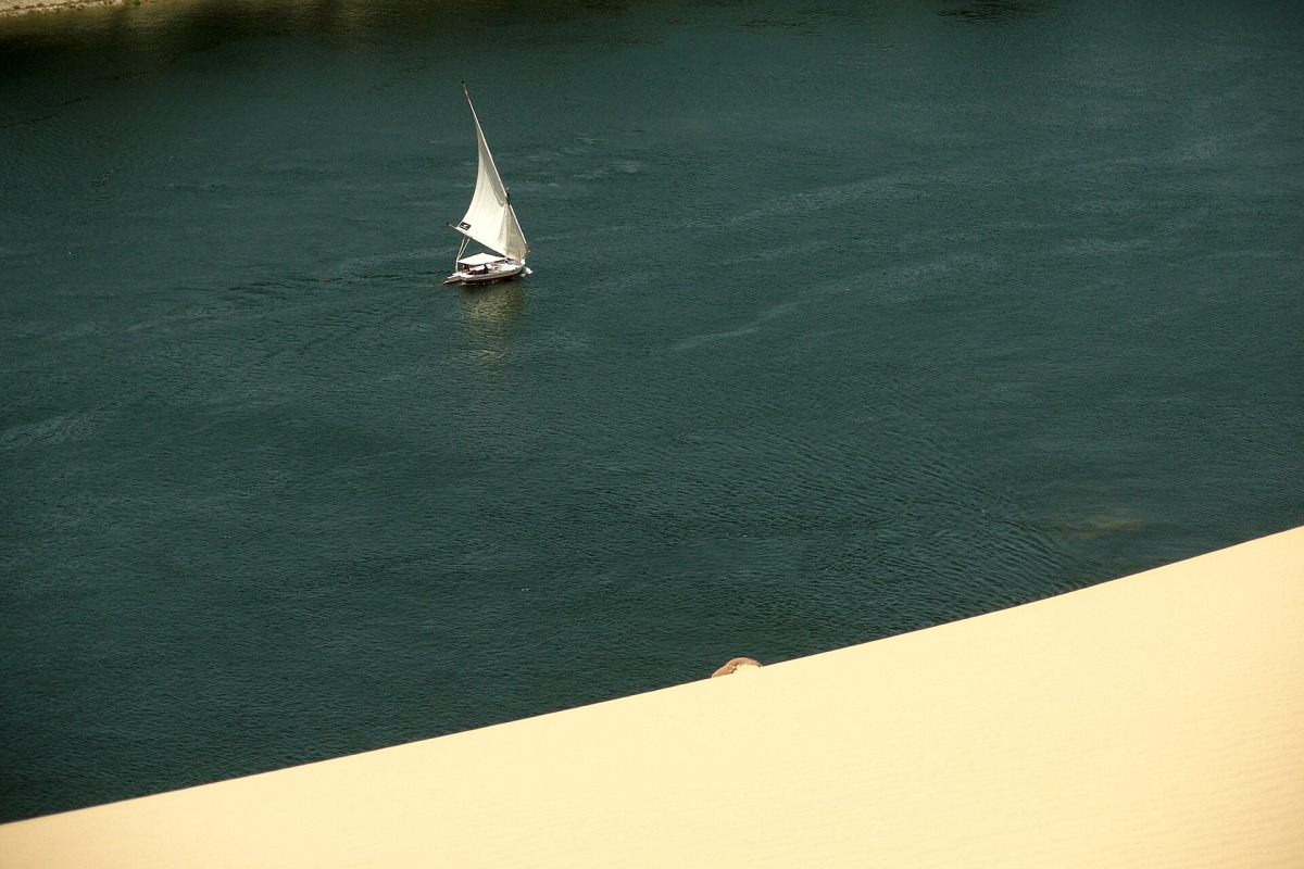 White-sailed felucca beside a golden dune at Aswan White-sailed felucca beside a golden dune at Aswan