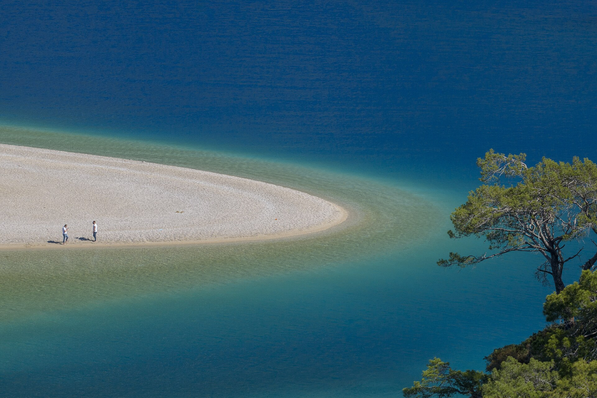 Pale beach curving into the blue water of Ölüdeniz lagoon