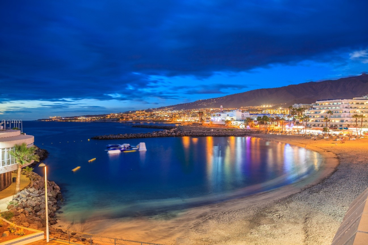 "Night view of a coastal promenade in the Canary Islands with bars and lights reflecting on the water"