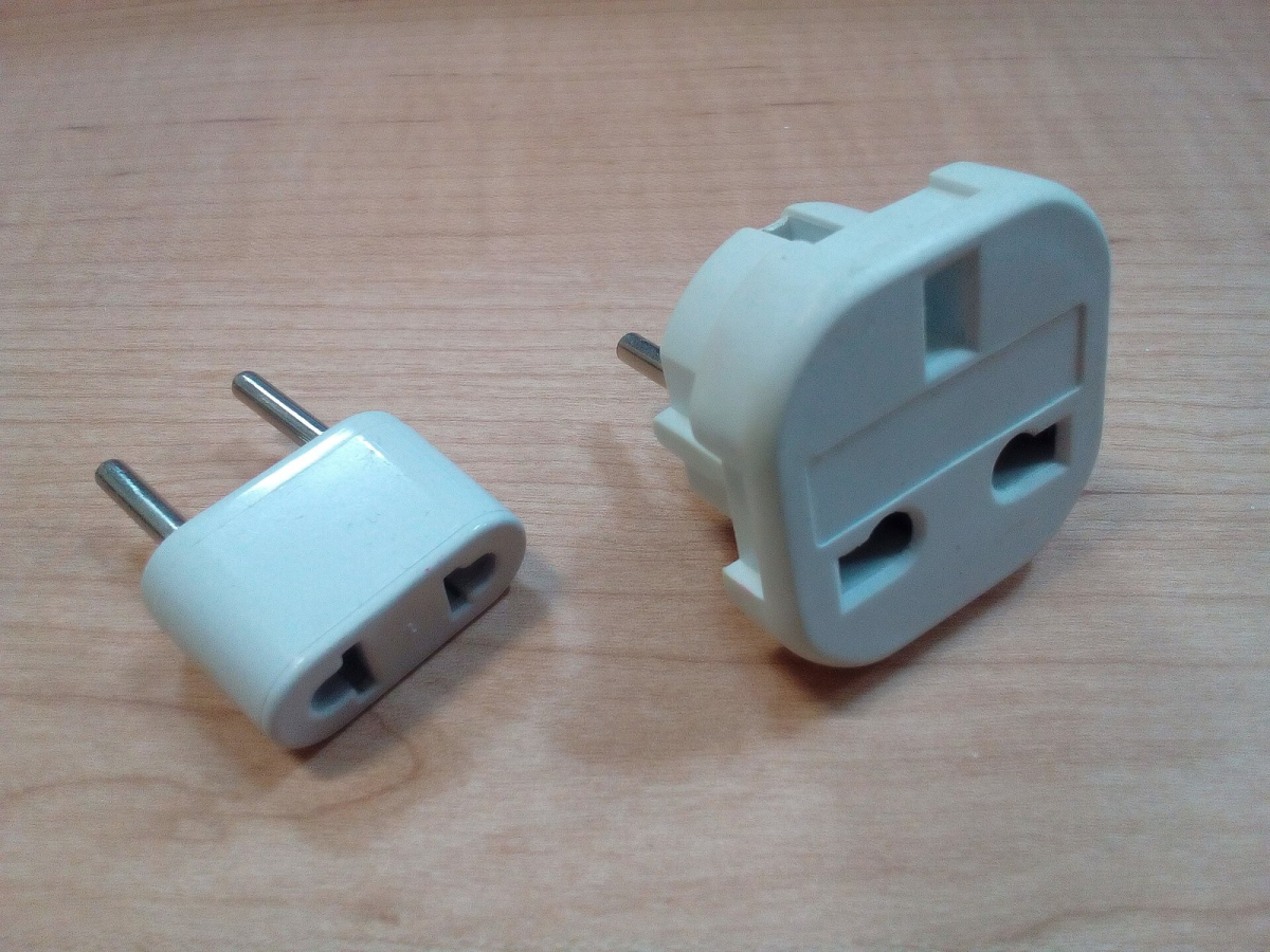 Two plug adaptors on a wooden surface Two plug adaptors on a wooden surface