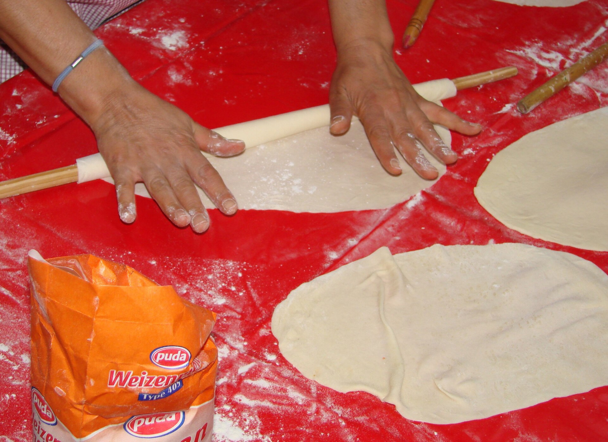 Hands rolling yufka dough around a thin wooden rolling pin