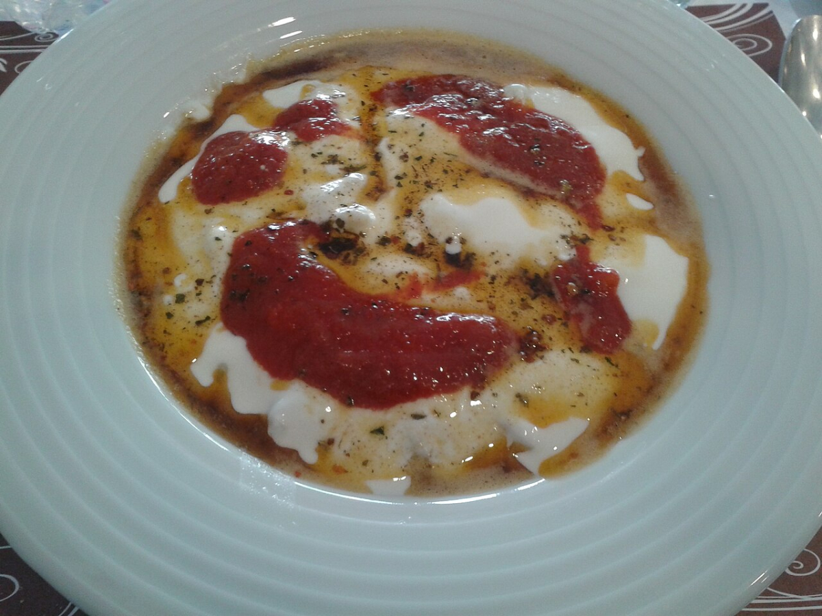 A plate of Turkish mantı covered with yogurt, tomato sauce and seasoned butter