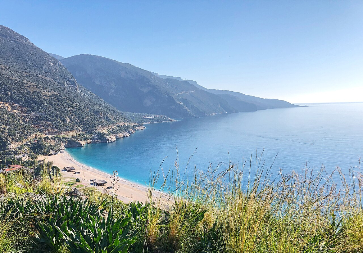 A sandy beach and blue sea below the mountains near Ölüdeniz