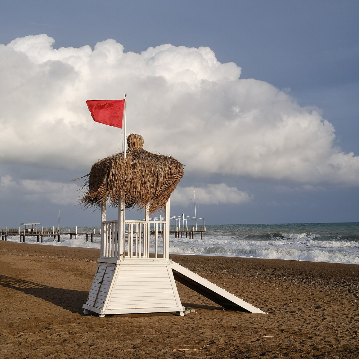 A red flag flying above a lifeguard tower beside rough water at Lara Beach, Antalya