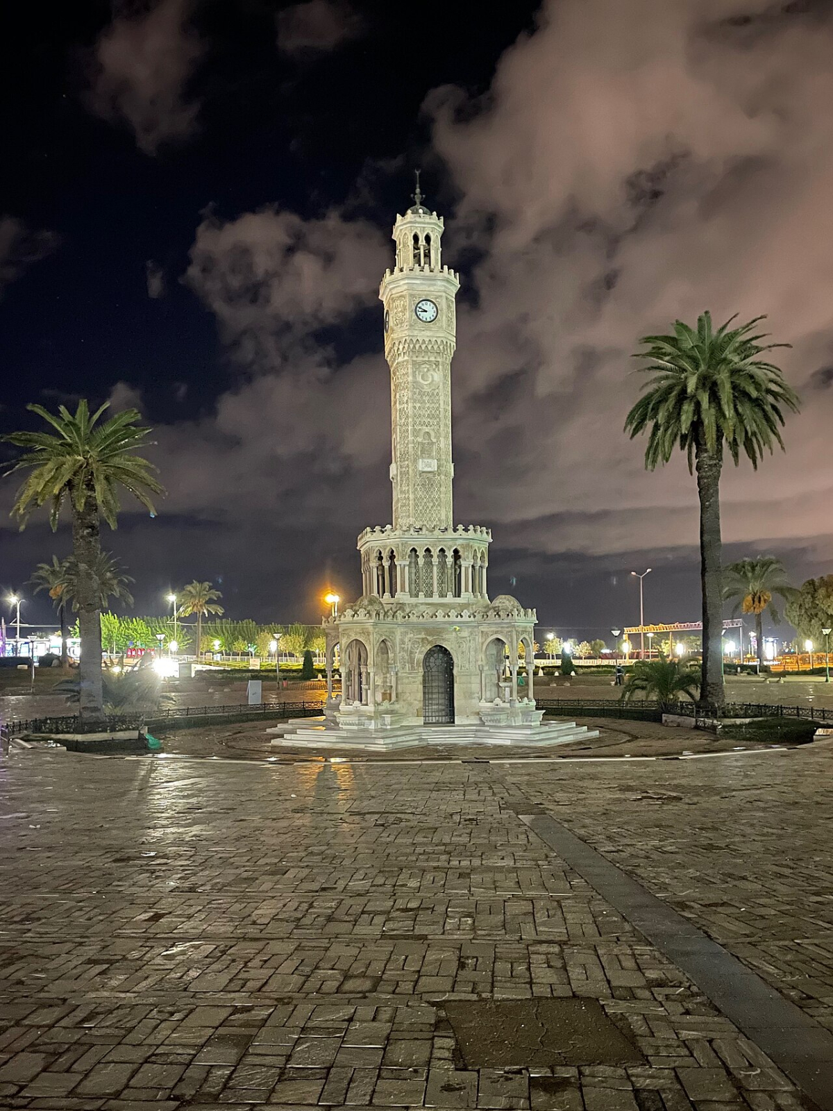 Illuminated İzmir Clock Tower and palm trees at night