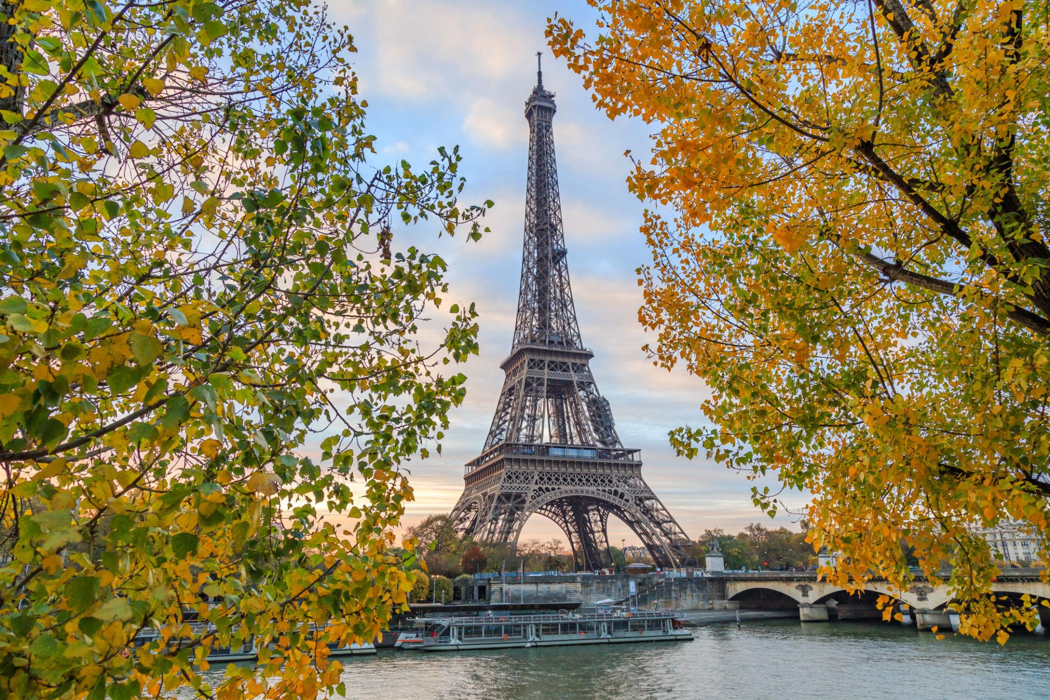 Best time to visit Paris during the autumn season Autumn view of the Eiffel Tower framed by colorful trees along the Seine River in Paris