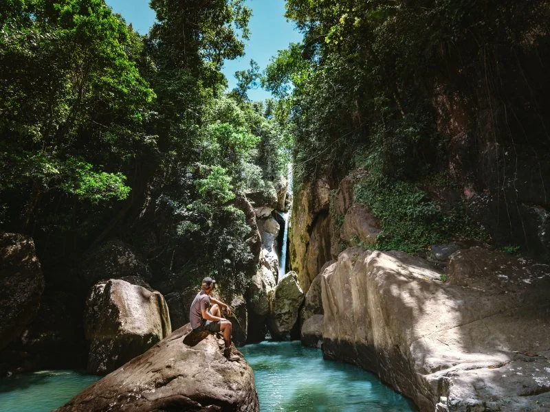Traveler enjoying a tropical river pool surrounded by lush forest in Puerto Rico, representing nature experiences and outdoor activities