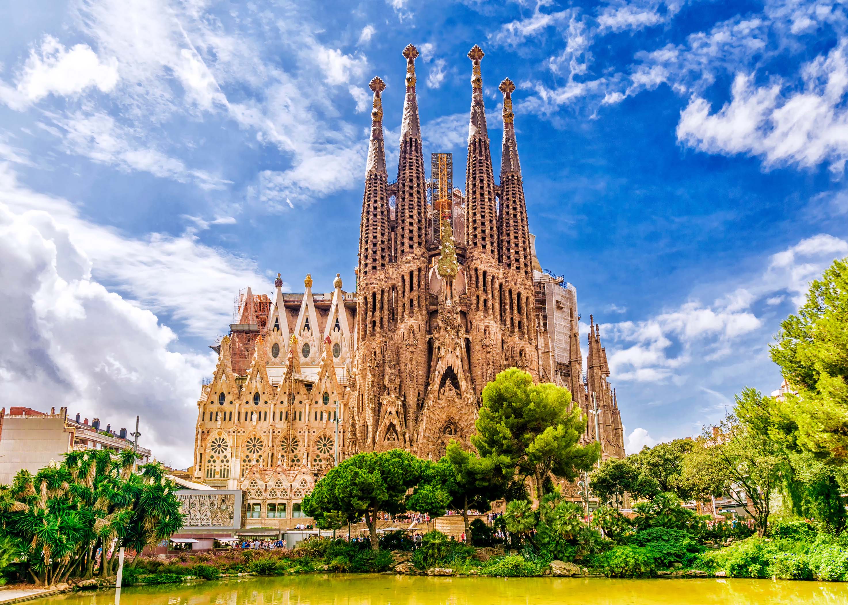 Sagrada Família basilica in Barcelona viewed from Plaça de Gaudí park with trees and reflection pool