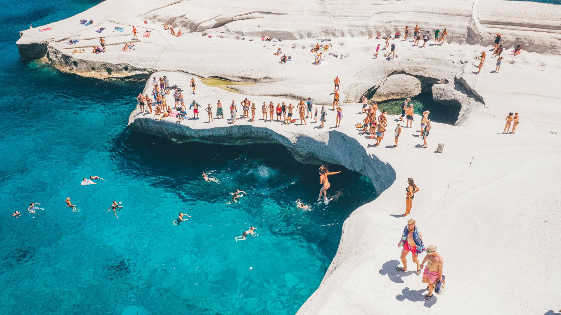Sarakiniko Beach in Milos, Greece Travelers swimming and relaxing on the white volcanic rocks of Sarakiniko Beach in Milos, Greece