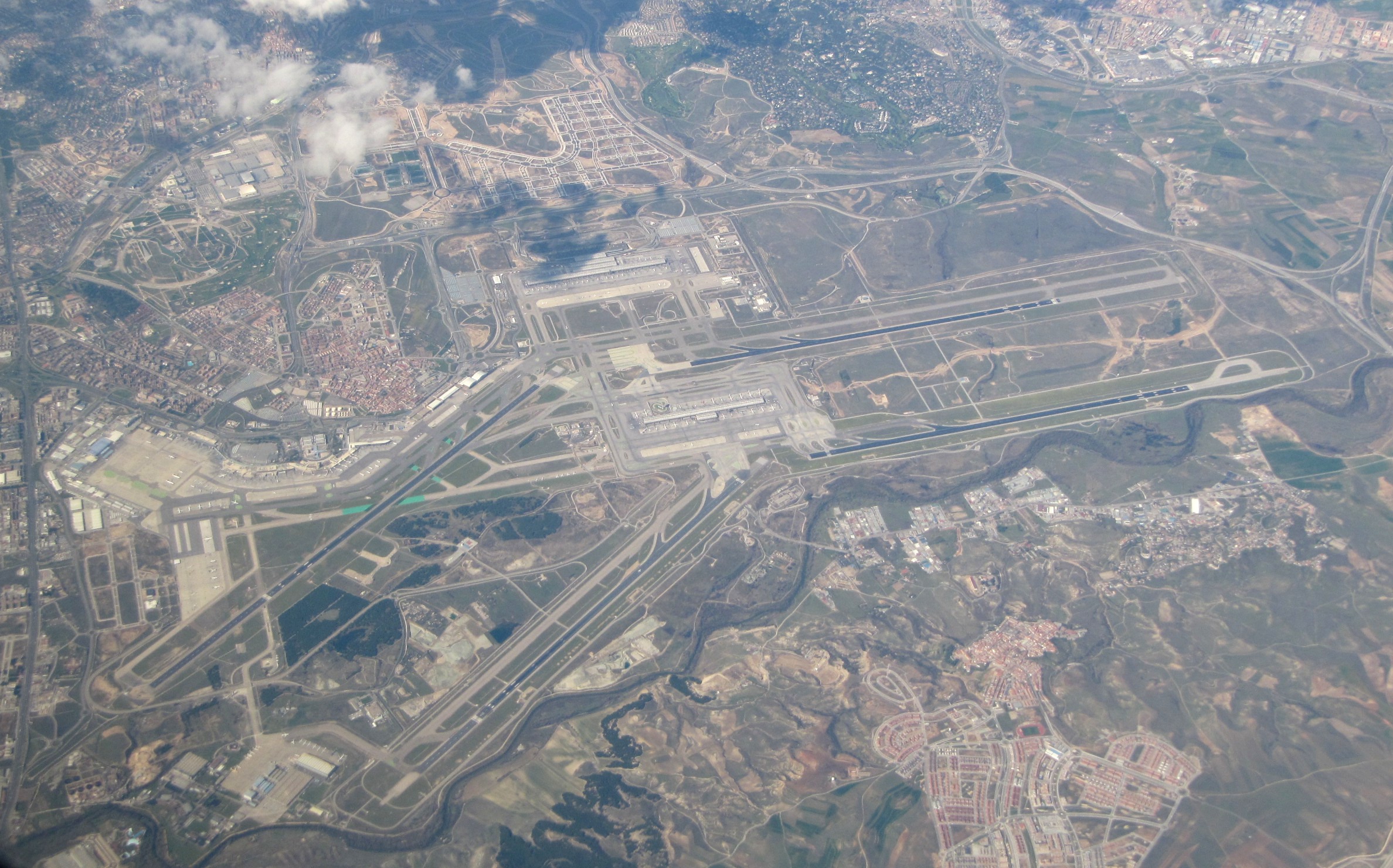 Aerial view of Madrid Barajas Airport terminal with aircraft, runways and city skyline in the background