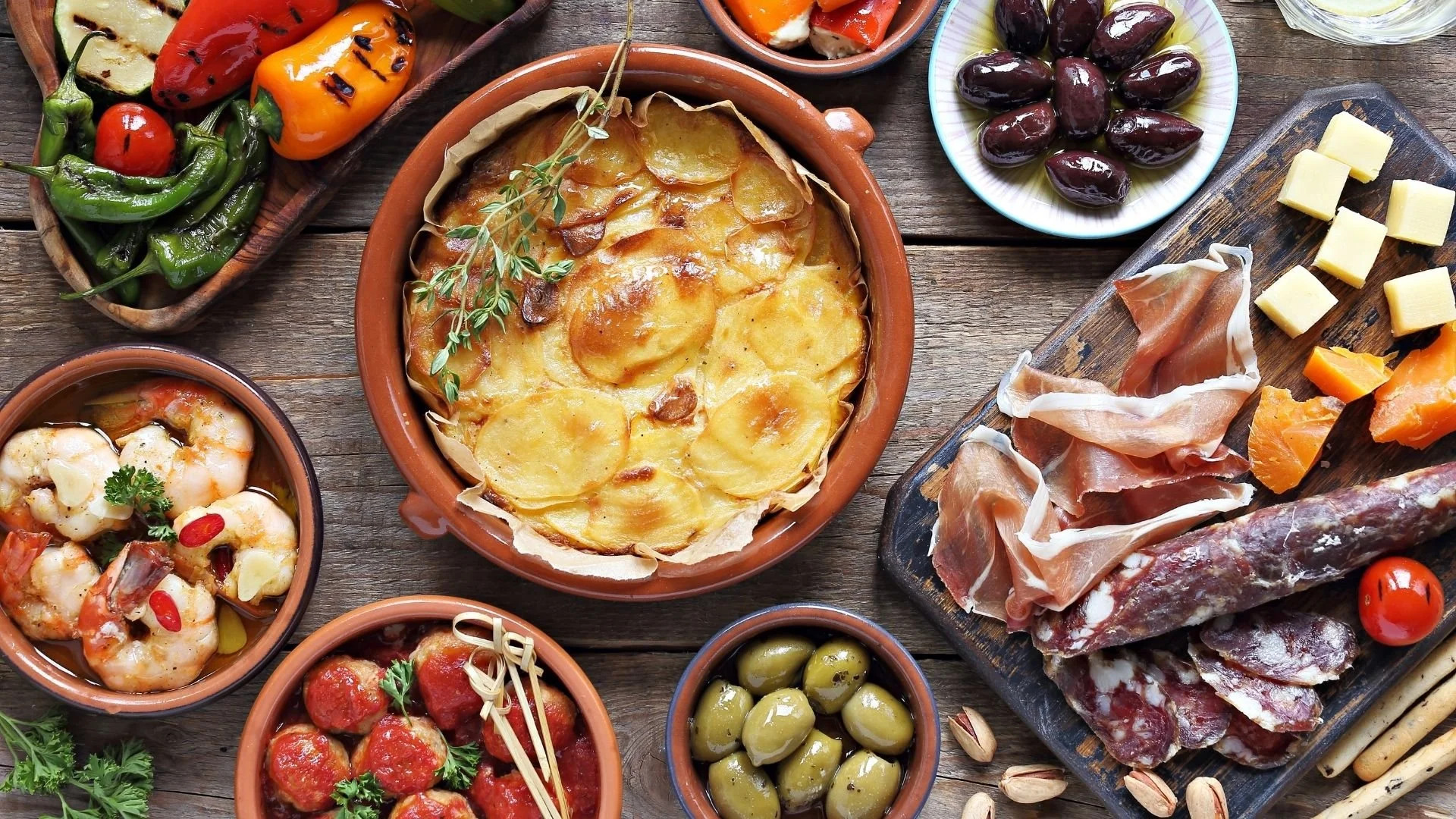Food & Drinks in Spain – Tapas, regional flavors and authentic Mediterranean cuisine Traditional Spanish tapas including garlic shrimp, patatas, jamón ibérico, chorizo, olives and grilled vegetables on a rustic wooden table