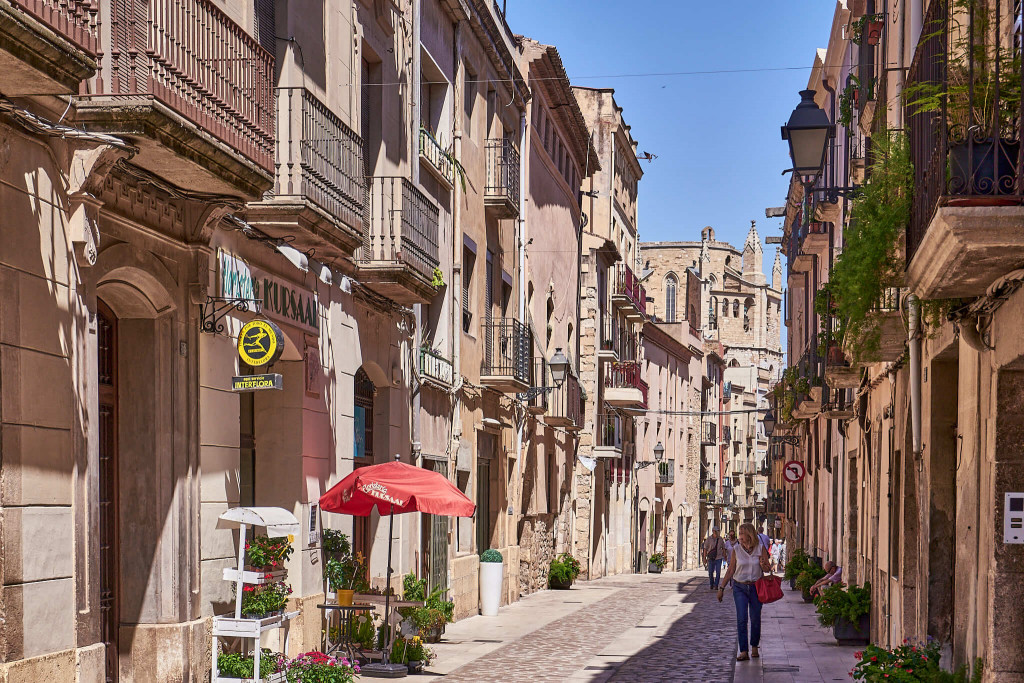A charming Spanish street with traditional Mediterranean architecture, local shops and people strolling on a sunny afternoon